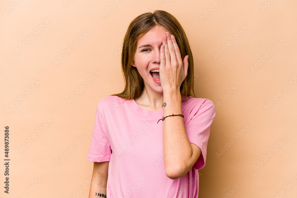 Young English woman isolated on beige background having fun covering half of face with palm. Young English woman isolated on beige background having fun covering half of face with palm.