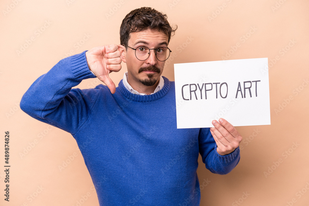 Young caucasian man holding a crypto art placard isolated on beige background showing a dislike gesture, thumbs down. Disagreement concept. Young caucasian man holding a crypto art placard isolated on beige background showing a dislike gesture, thumbs down. Disagreement concept.