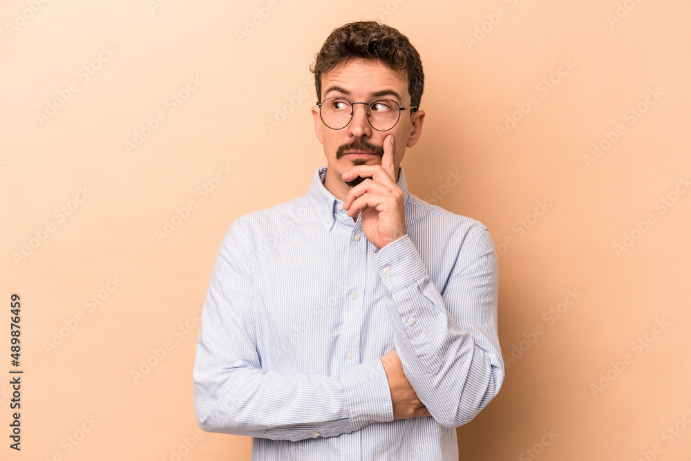 Young caucasian man isolated on beige background contemplating, planning a strategy, thinking about the way of a business. Young caucasian man isolated on beige background contemplating, planning a strategy, thinking about the way of a business.