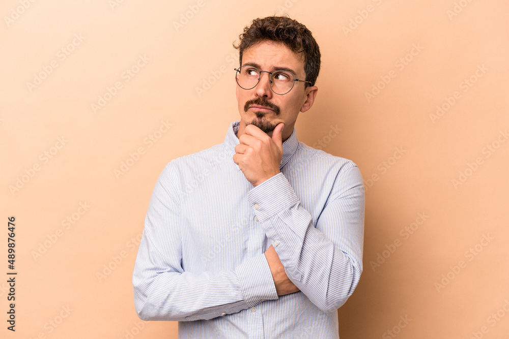 Young caucasian man isolated on beige background thinking and looking up, being reflective, contemplating, having a fantasy. Young caucasian man isolated on beige background thinking and looking up, being reflective, contemplating, having a fantasy.