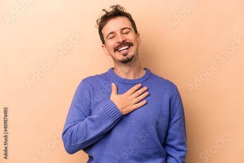 Foto Young caucasian man isolated on beige background laughs out loudly keeping hand on chest