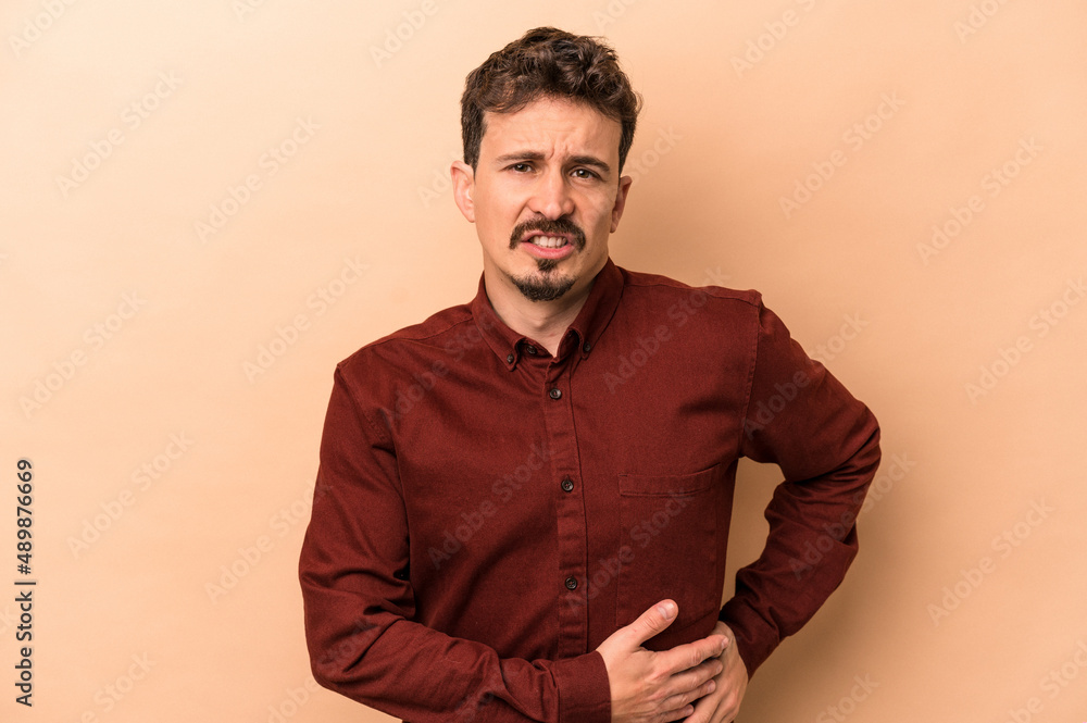 Young caucasian man isolated on beige background having a liver pain, stomach ache. Young caucasian man isolated on beige background having a liver pain, stomach ache.