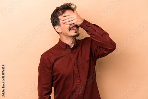 Young caucasian man isolated on beige background laughs joyfully keeping hands on head. Happiness concept.