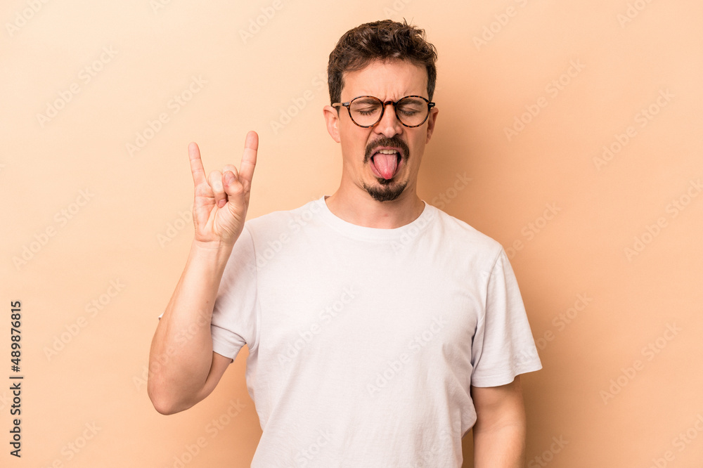 Young caucasian man isolated on beige background showing rock gesture with fingers Young caucasian man isolated on beige background showing rock gesture with fingers