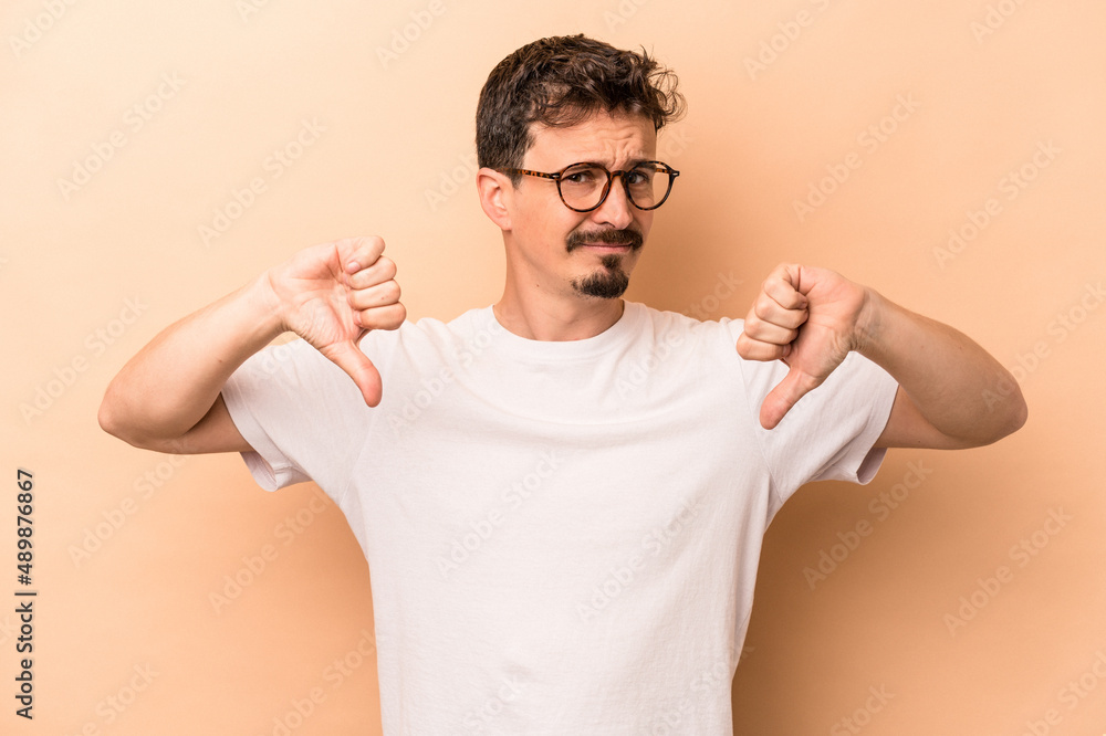 Young caucasian man isolated on beige background showing thumb down, disappointment concept. Young caucasian man isolated on beige background showing thumb down, disappointment concept.