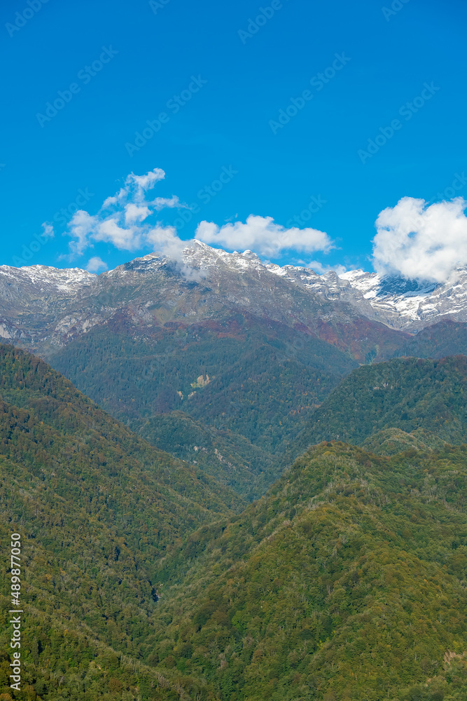 Beautiful green mountains with snowy peaks on a sunny day. Beautiful mountain landscape. Vertical photo
