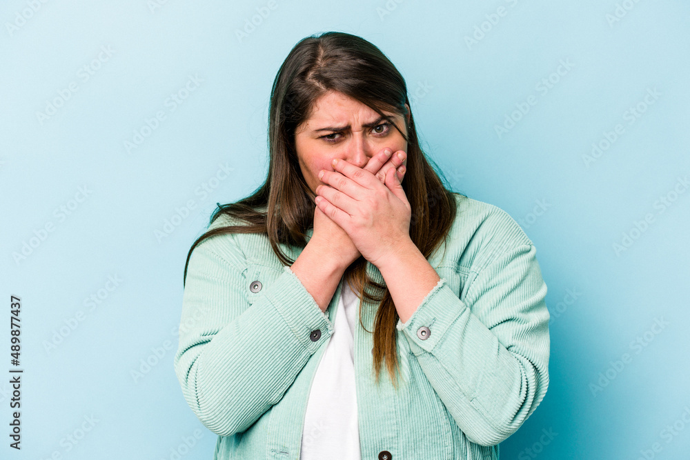Young caucasian overweight woman isolated on blue background covering mouth with hands looking worried. Young caucasian overweight woman isolated on blue background covering mouth with hands looking worried.