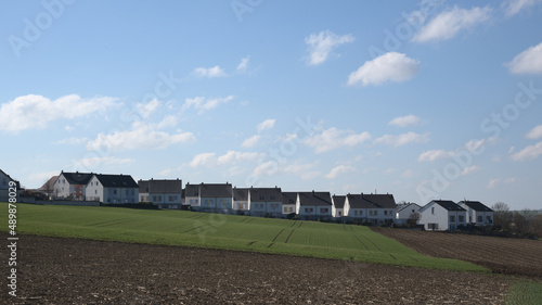 A row of newly built semi- detached houses on the horizon with blue cloudy sky.