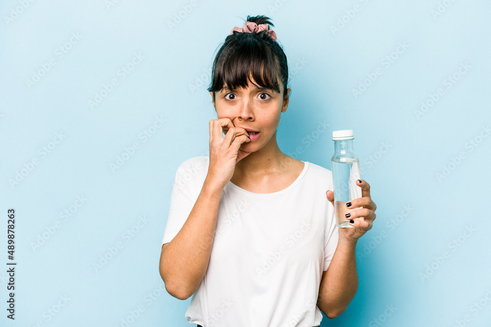 Young hispanic woman holding a bottle of water isolated on blue background biting fingernails, nervous and very anxious. Young hispanic woman holding a bottle of water isolated on blue background biting fingernails, nervous and very anxious.