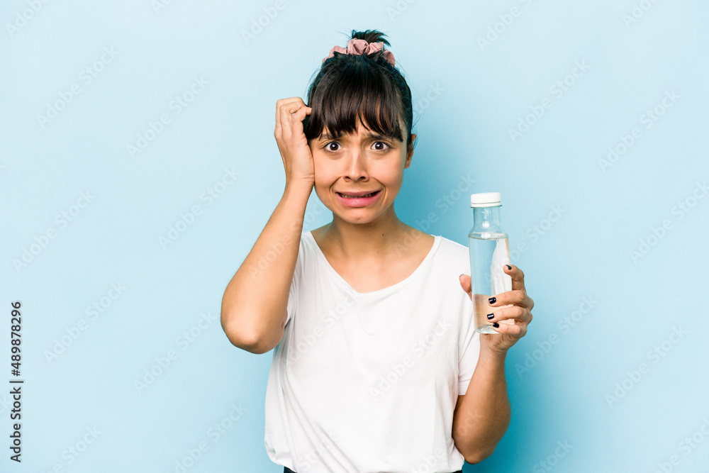 Young hispanic woman holding a bottle of water isolated on blue background being shocked, she has remembered important meeting.