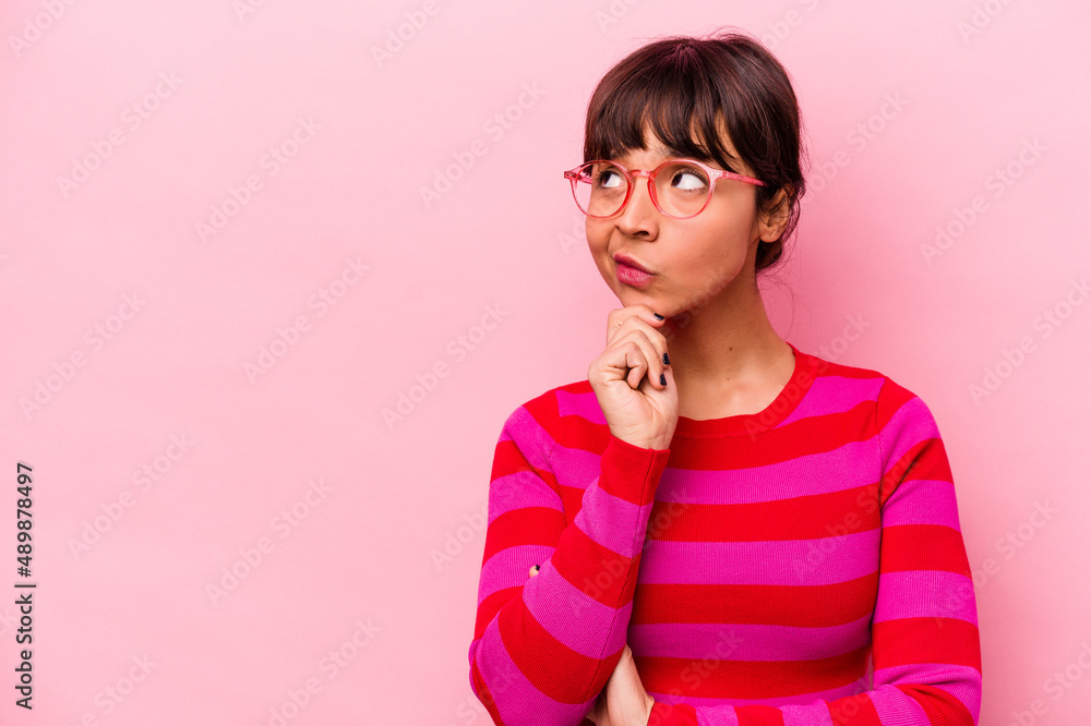 Young hispanic woman isolated on pink background looking sideways with doubtful and skeptical expression.