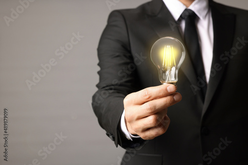 Glow up your ideas. Closeup view of businessman holding light bulb on grey background, space for text