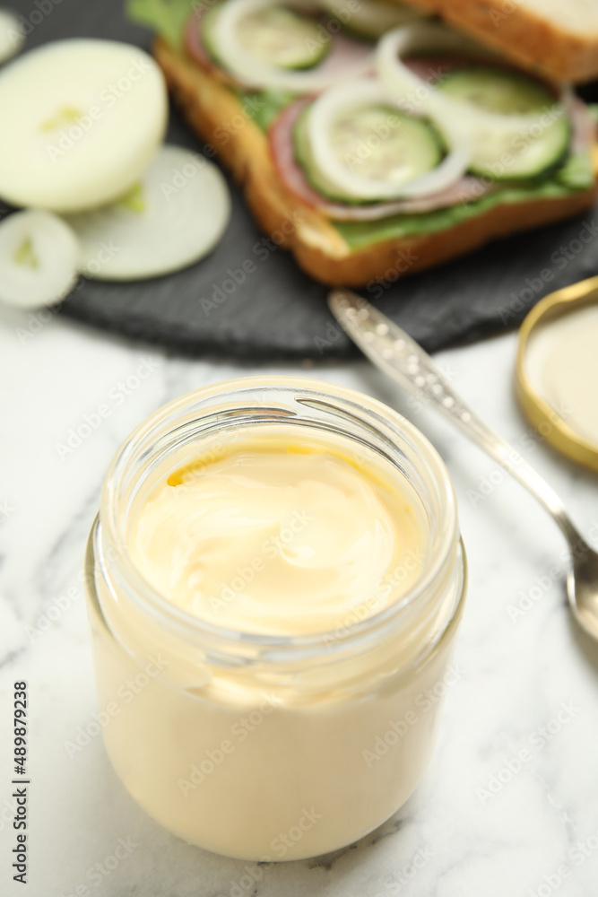 Jar of delicious mayonnaise near fresh sandwich on white marble table Jar of delicious mayonnaise near fresh sandwich on white marble table