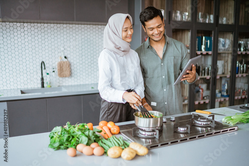 muslim couple cooking together in the kitchen while look at video