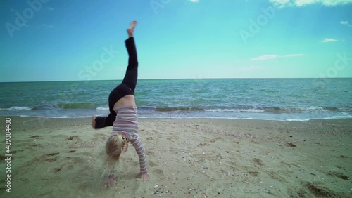 Little child girl making cartwheel acrobatic movement on a bach by the sea photo
