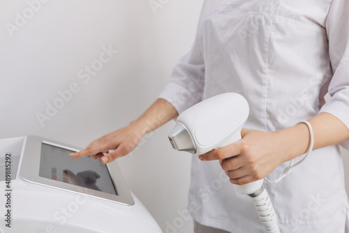 A woman tunes a laser hair removal machine. Girl holding a working part of the epilator in her hands in a modern beauty salon. Underarm Laser Hair Removal concept
