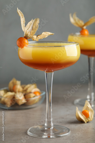 Tasty cocktail decorated with physalis fruits on grey table