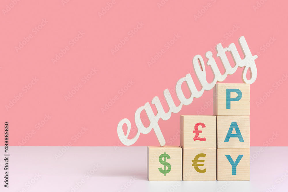 The concept of equal pay. The word equality stands on wooden cubes with dollar, euro and pound symbols. The concept of equal pay. The word equality stands on wooden cubes with dollar, euro and pound symbols.