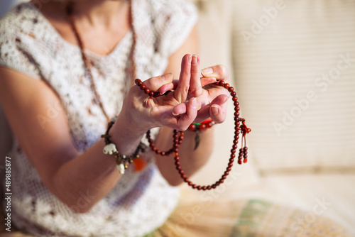 Woman at meditate place in lotus position using Mudra, hand close up, strands of beads used for keeping count during mantra meditations