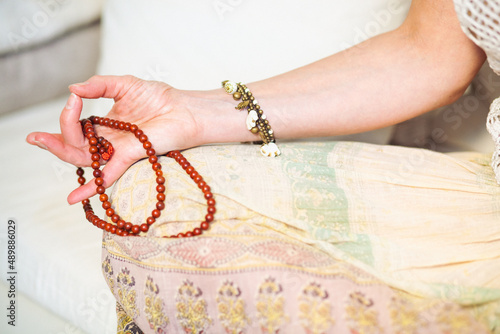 Woman at meditate place in lotus position using Mudra,  hand close up, strands of  beads used for keeping count during mantra meditations