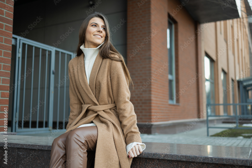 Fototapeta premium Beautiful woman in a brown coat sits in the middle of the street