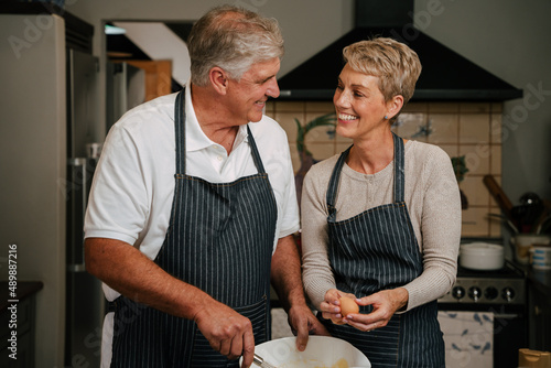 Caucasian elderly couple smiling at each other baking in kitchen