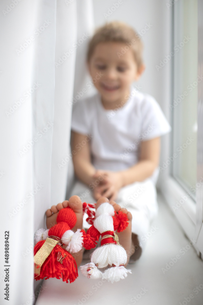 Cute child, blond boy, playing with white and red bracelet, martenitsa Cute child, blond boy, playing with white and red bracelet, martenitsa