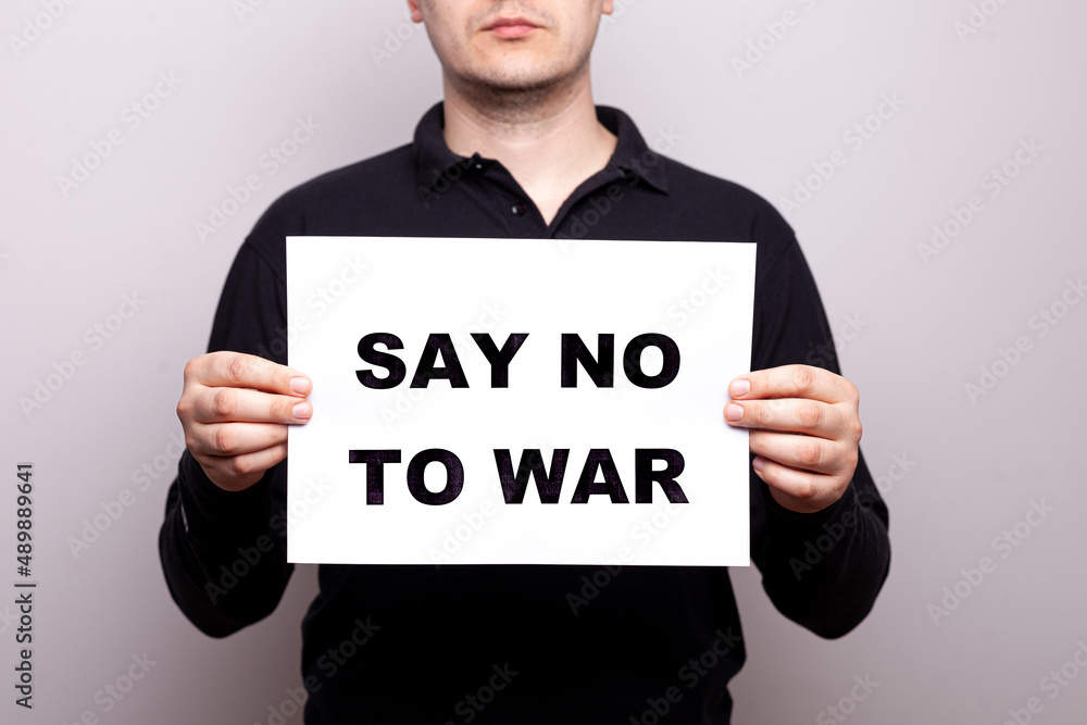 say no to war. a man holds a poster in his hands with appeals, a message not to use aggression. no war. a man in black clothes on a white background, close-up without a face say no to war. a man holds a poster in his hands with appeals, a message not to use aggression. no war. a man in black clothes on a white background, close-up without a face