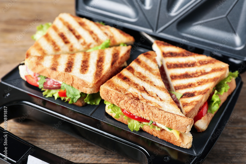 Modern grill maker with sandwiches on wooden table, closeup Modern grill maker with sandwiches on wooden table, closeup