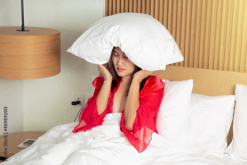 Female in a satin red nightgown lying on bed and closing her head with the pillow at night. Asian woman suffering from insomnia or depression. Female in a satin red nightgown lying on bed and closing her head with the pillow at night. Asian woman suffering from insomnia or depression.