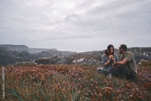 Happy young loving couple sitting in a meadow of flowers and plants, smelling the flowers, green and military scout style.