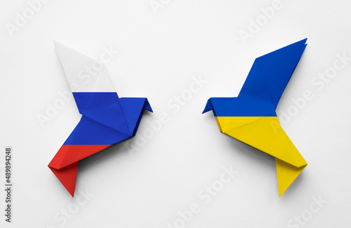 Two origami paper doves in the colors of the flags of Russia and Ukraine on a white background. The concept of peace between two states