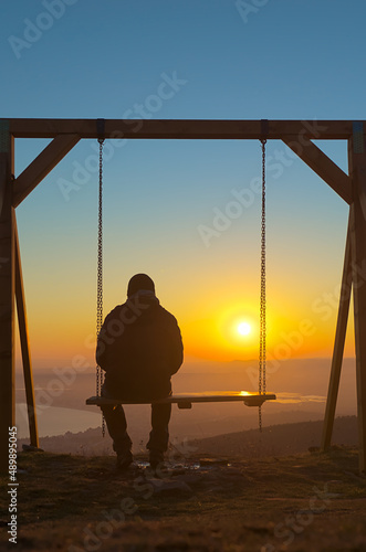A man and a child are sitting on a swing on a hill overlooking a beautiful landscape at sunset, the sea and the valley