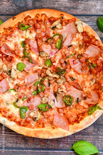 Close up of classic italian pizza with ham. Fresh basil,tomato sauce ,mozzarella cheese , mushrooms and green peppers