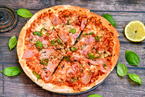  Close up of   classic  italian pizza   with ham. Fresh basil,tomato sauce ,mozzarella cheese , mushrooms and  green peppers