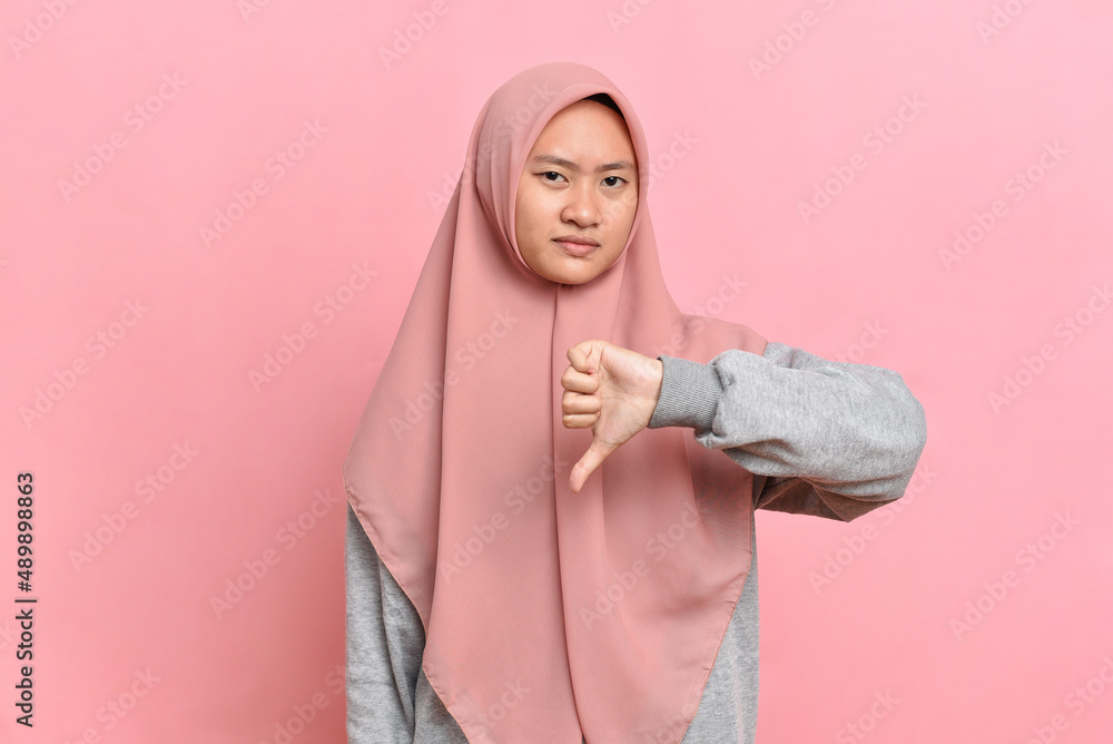 Fototapeta premium Asian Muslim woman disappointed showing thumb down dislike gesture