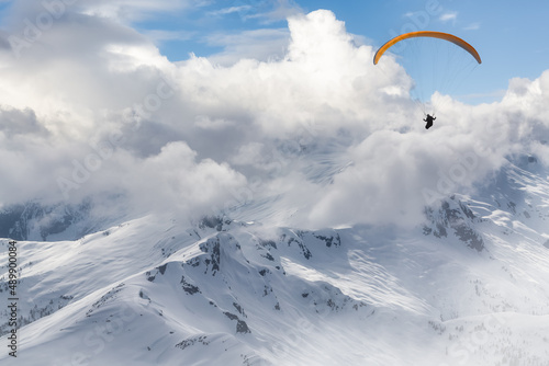 Adventure Composite Image of Paraglider Flying up high in the Rocky Mountains. Cloudy Sky. Aerial Background from British Columbia, Canada. Extreme Sport Concept. winter