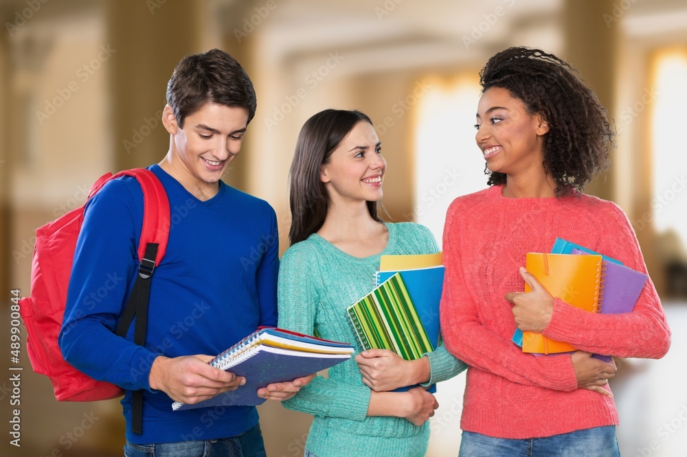 Attractive college friends smiling and hugging while carrying notebooks at class Attractive college friends smiling and hugging while carrying notebooks at class