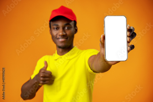African courier guy showing smartphone with blank screen and holding box in studio
