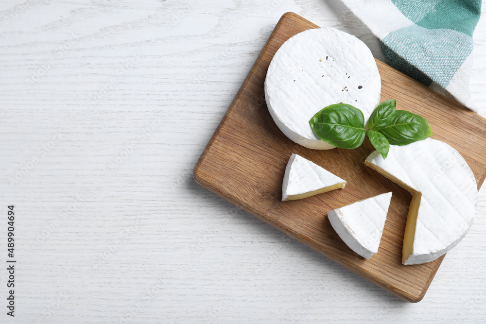 Tasty cut and whole brie cheeses with basil on white wooden table, flat lay. Space for text Tasty cut and whole brie cheeses with basil on white wooden table, flat lay. Space for text
