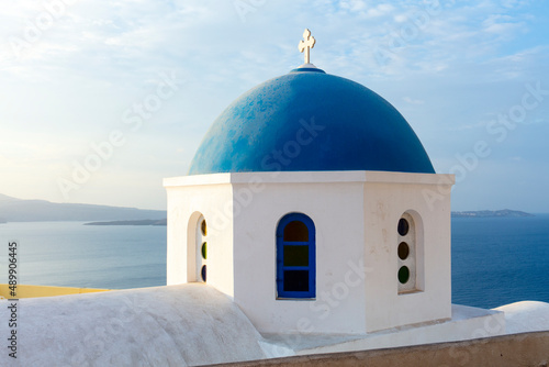 White church with blue dome roof overlooking Aegean sea on Santorini, Greece.