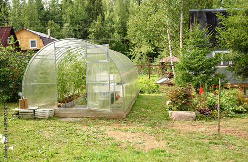 Greenhouse in the backyard with an open door. Growing tomatoes and cucumbers in the summer in your garden