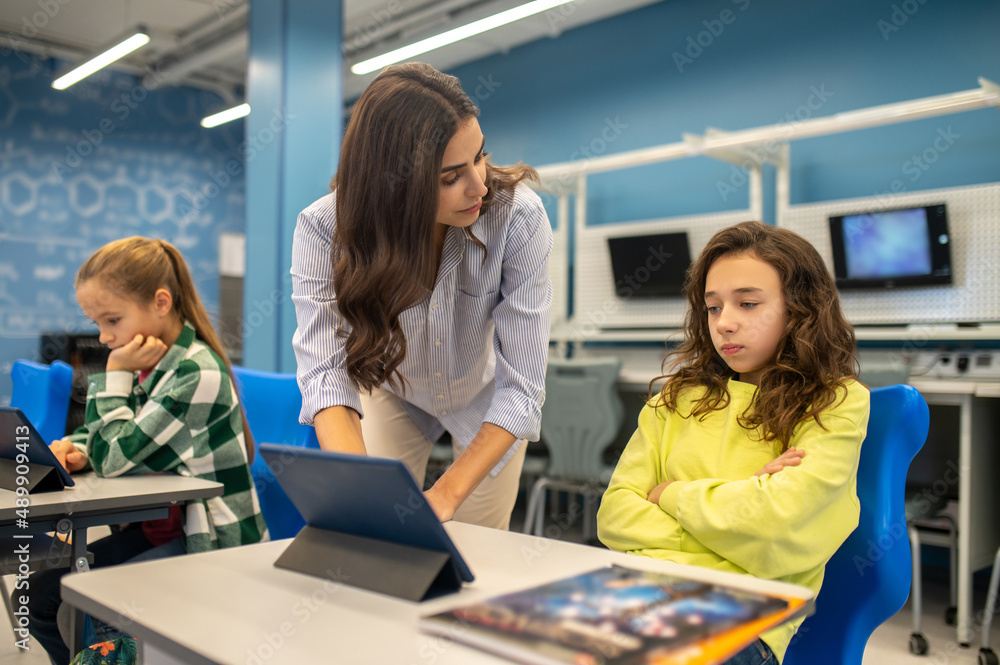 Teacher standing near sad girl sitting at desk Teacher standing near sad girl sitting at desk