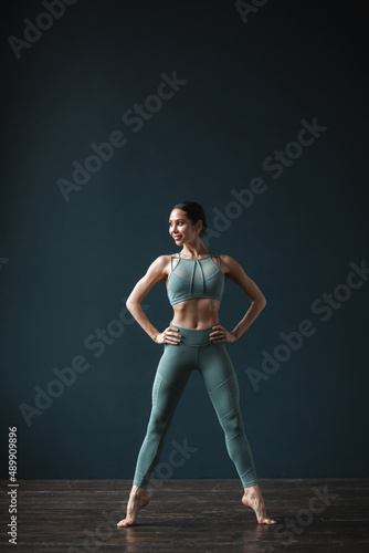 Beautiful fitness woman with perfect fit body in sportswear for training in full length on a dark background.