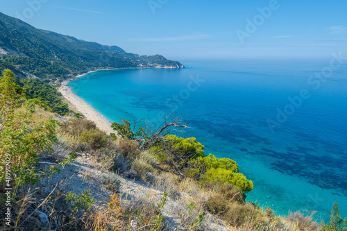 Scenic cliffs near sunny sea shore on a bright clear blue day in Greece. Pefkoulia beach with turquoise water and clear blue sky, Lefkada island, Ionian sea coast