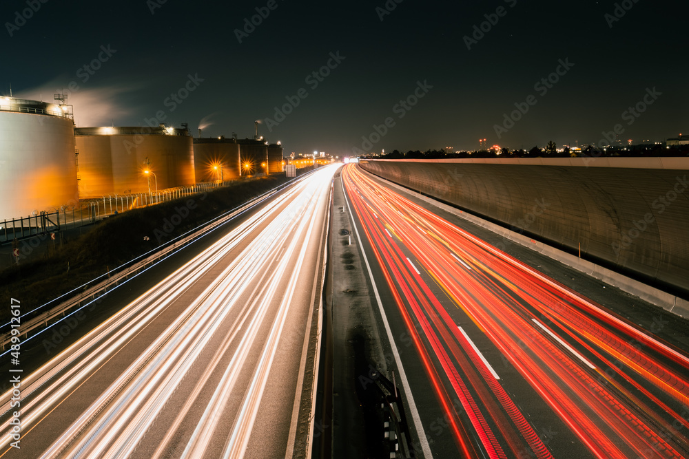 Light trails after long exposure of car traffic on a highway next to industry buildings and a noise barrier at night 