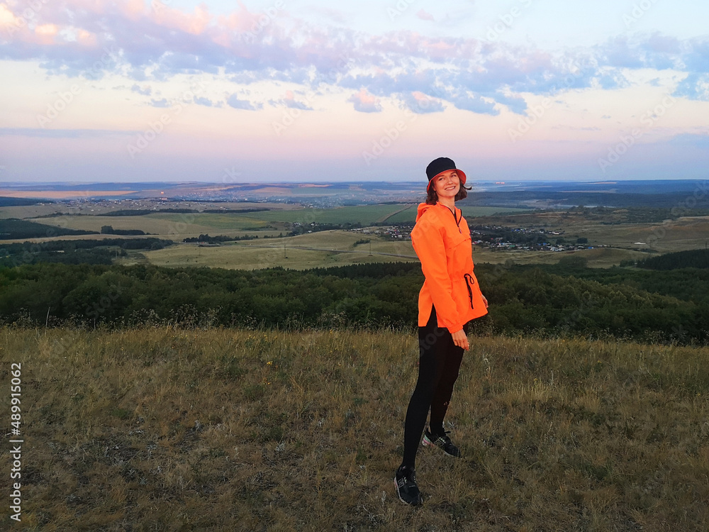 Beautiful smiling girl outdoors in a bright orange sports jacket. Concept of travel, sport, freedom, happiness.