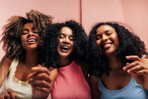 Three happy girlfriends with curly hair laughing together and looking at camera photo