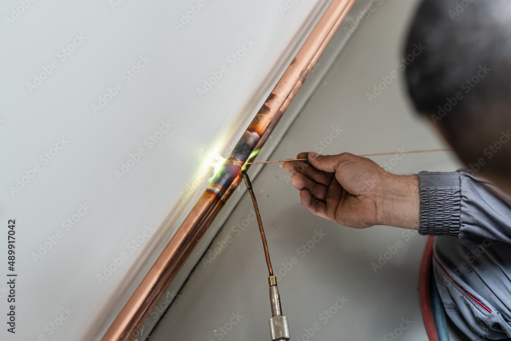 Unknown industrial worker plumber with central heating copper pipes welding using gas torch or blowtorch on the wall in house building or apartment - real people at work copy space