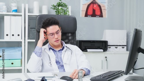 Wallpaper Mural Stressed and overworked Asian male doctor sitting on table in hospital Torontodigital.ca